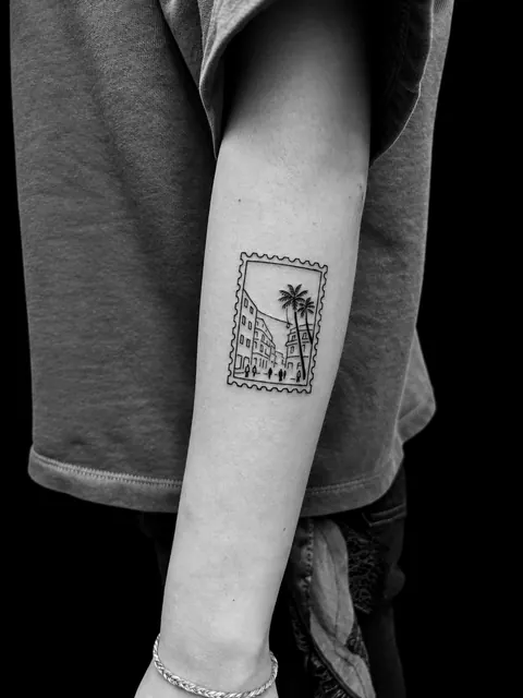 Tatuaje en forma de sello postal con una calle de Málaga y palmeras en un antebrazo