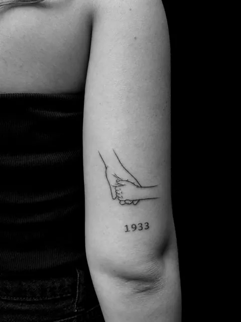 Tatuaje fine line de dos manos entrelazadas sobre el año 1933 en un brazo