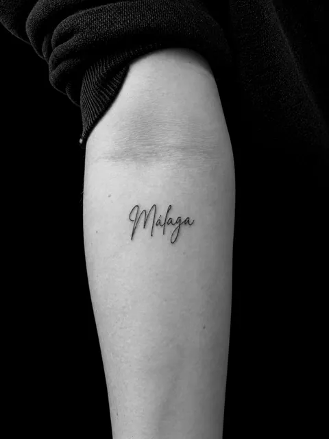 Tatuaje de letra cursiva con la palabra «Málaga» en un antebrazo