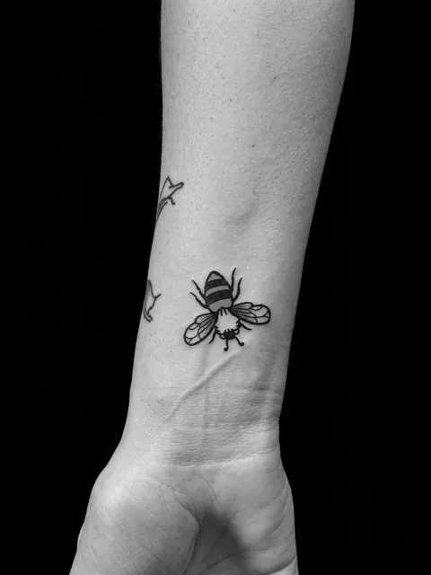 Tatuaje fine line de una abeja en una muñeca