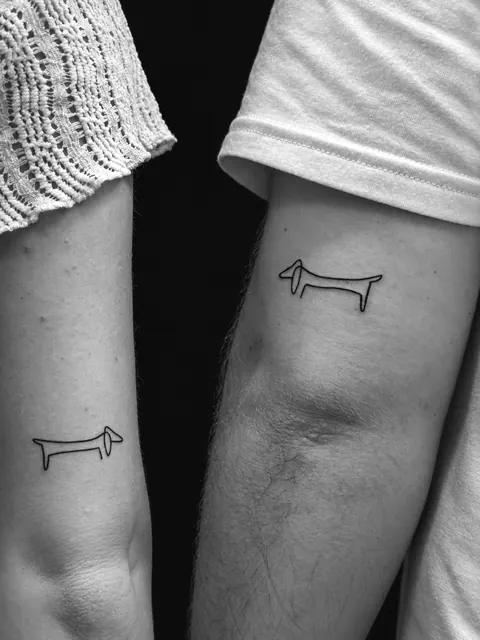 Tatuajes a juego de un teckel de una sola línea, al estilo de Picasso, en los brazos de dos personas