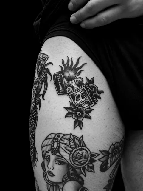 Tatuaje tradicional de un mechero en llamas con una calavera y flores en un muslo, entre otros flashes