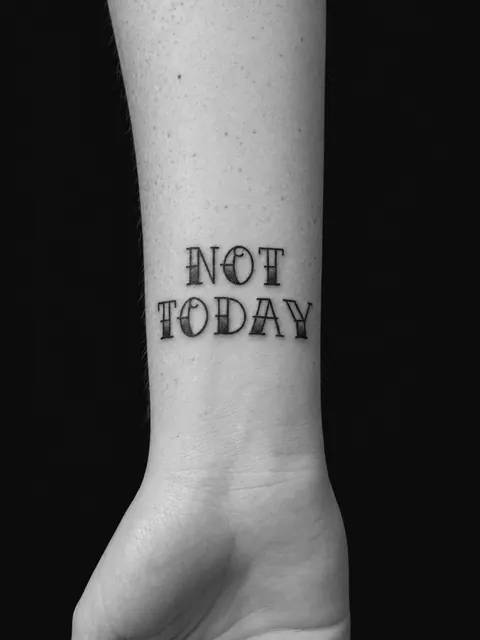 Tatuaje de lettering de estilo tradicional con la frase «Not today» sobre la muñeca