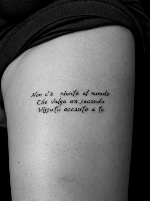 Tatuaje de un verso en italiano escrito a mano en tres líneas en la parte superior del brazo