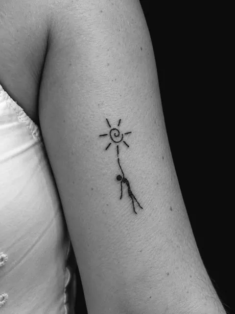 Pequeña figura que sostiene una línea hacia un sol en espiral, en la parte superior del brazo