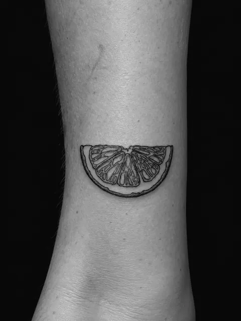 Tatuaje fine line de una rodaja de limón sobre un tobillo