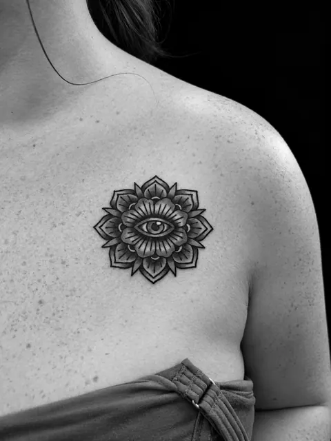 Tatuaje tradicional de un ojo dentro de una flor simétrica, bajo la clavícula