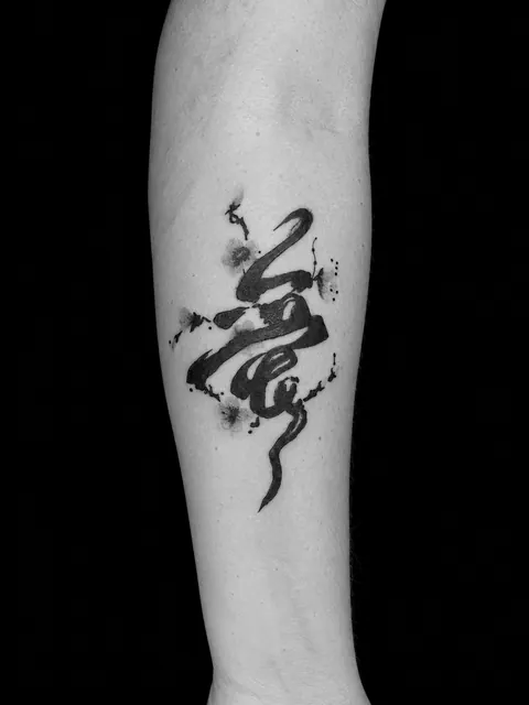 Tatuaje de lettering con una pincelada de tinta negra y flores de cerezo rosas en un antebrazo