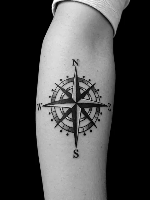Tatuaje ilustrativo de una rosa de los vientos con sombreado en un antebrazo