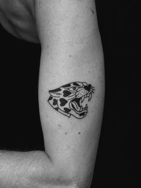 Tatuaje tradicional de una cabeza de leopardo con manchas en forma de corazón en un antebrazo