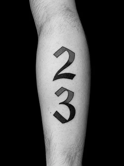 Tatuaje de lettering con los números 23 en rojo y negro en un gemelo