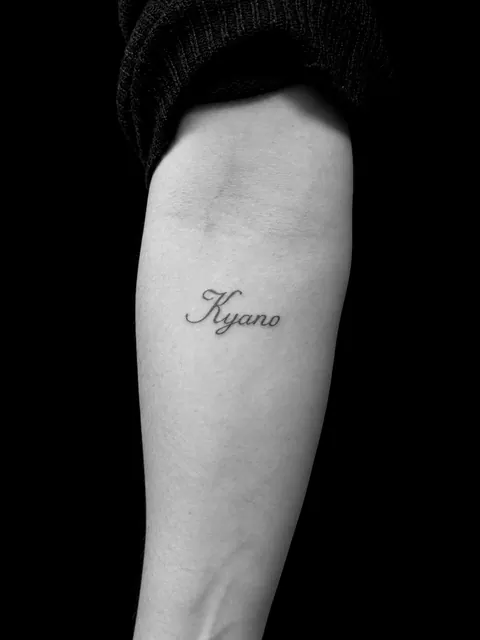 Tatuaje de lettering cursivo con el nombre «Kyano» en tinta roja en un antebrazo