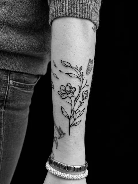 Tatuaje de línea fina de una rama de flores con una mariposa en un antebrazo