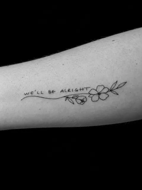 Frase «We’ll be alright» que termina en una pequeña flor, en un antebrazo