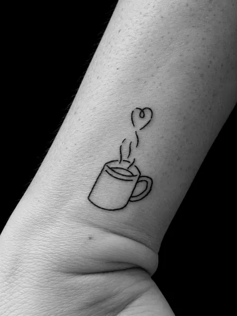 Tatuaje de línea fina de una taza de café cuyo vapor termina en un corazón, en un antebrazo