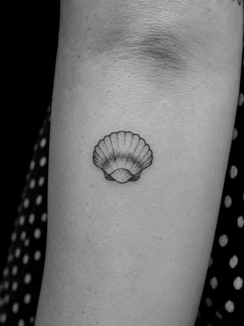 Tatuaje pequeño de una concha de vieira con sombreado de puntos en la parte interior del brazo