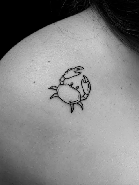 Tatuaje pequeño de un cangrejo de línea fina con un sombreado ligero en un hombro